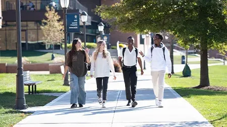 Four students with backpacks walking and talking along sidewalk.